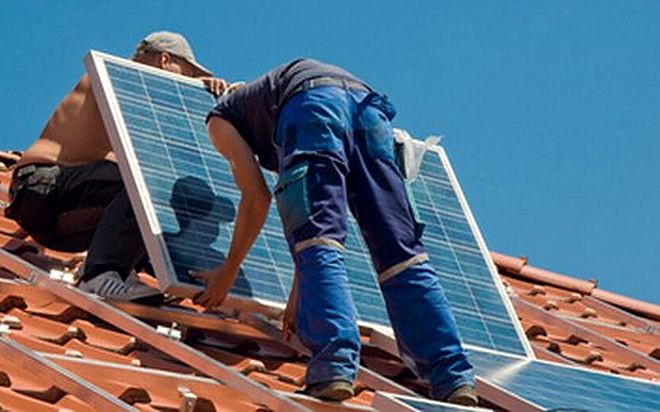 Zwei Monteure tragen ein Solarmodul über ein Ziegeldach