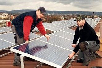 Zwei Monteure richten ein Solarmodul auf einem Flachdach aus