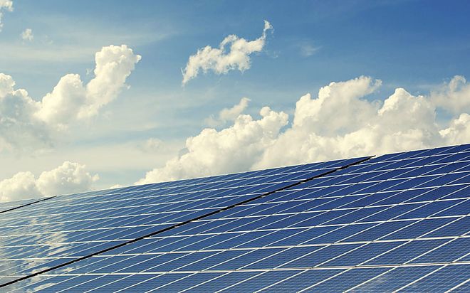 Reihe aufgeständerter Solarmodule vor einem Himmel mit Quellwolken