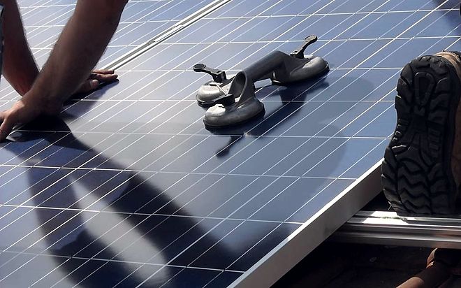 Monteur setzt mit zwei Saughebern ein Solarmodul auf die Unterkonstruktion